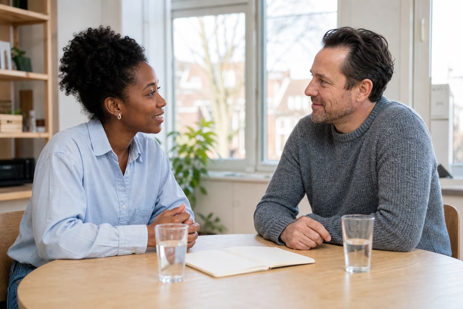 Twee mensen aan een tafel in gesprek, met water en een open notitieboek